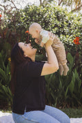 A parent smiling and lifting their baby up outdoors in a garden